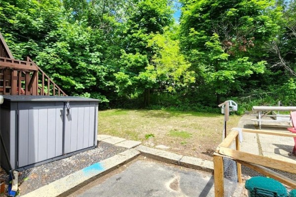 A grey storage shed sits on gravel beside a grassy backyard with trees. - 50 Albany Street, Sudbury