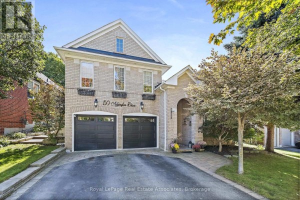 Close-up front view of a two-story light brick house with a double garage and arched entryway. - 50 Arborglen Drive, Halton Hills