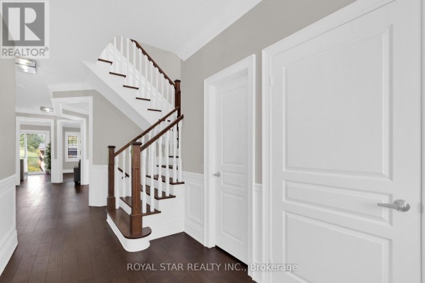 Interior entryway with dark wood floors, white wainscoting, and a dark wood staircase. - 50 Brookwater Crescent, Caledon