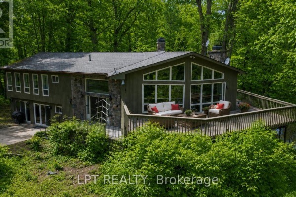 Exterior front view of a two-story green house with large windows and a stone section. - 50 Concession Rd 2 W, Tiny