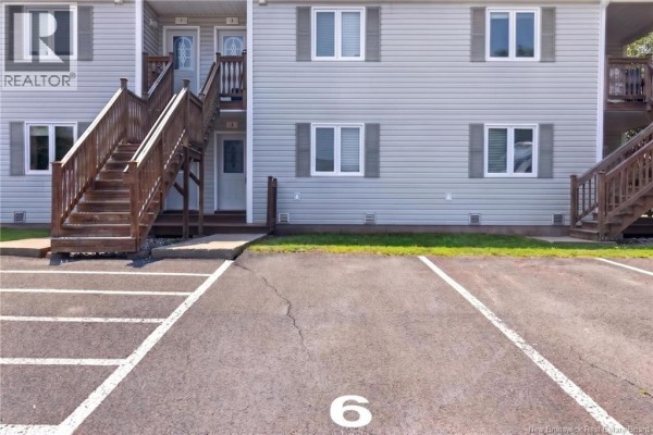 Close-up of the numbered parking space 6 in front of a grey apartment building. - 50 Damien Street Unit# 6, Dieppe