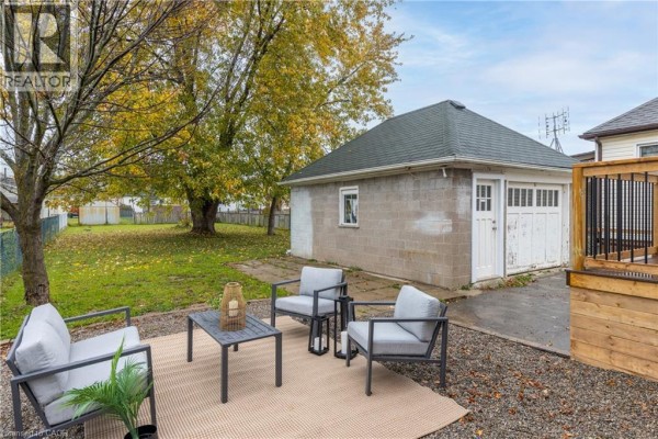 Living room with a sofa, coffee table, and armchair, adjacent to a hallway with a glass door. - 50 Fifth Street, Welland