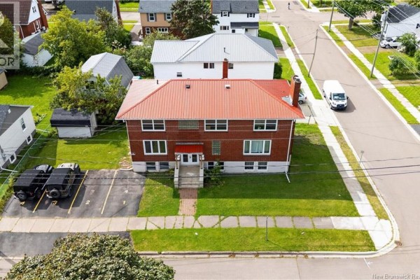 Rear aerial view of the brick multi-family building with a red metal roof and parking lot. - 50 Leslie, Moncton