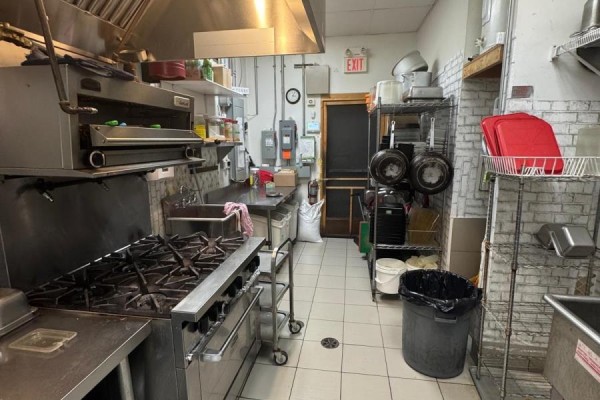 Commercial kitchen with gas range, oven, stainless steel counters, sinks, and storage shelving. - 50 Market Street S, Brantford