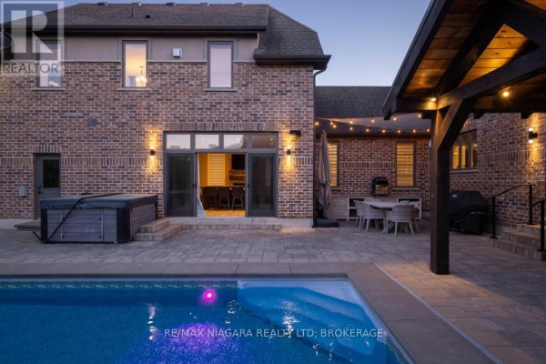 Backyard pool area with a covered outdoor entertainment space, hot tub, and seating at dusk. - 50 Sandalwood Crescent, Niagara On The Lake