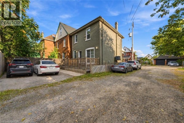Rear exterior view of the house with a wooden deck, gravel driveway, and parking for multiple vehicles. - 50 Somerset Avenue, Hamilton