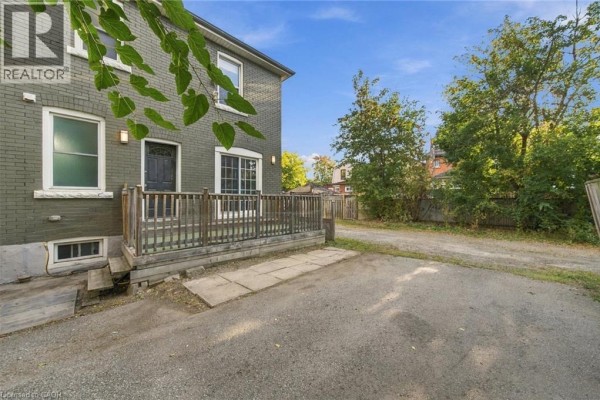 Back entrance to the house with a small wooden deck and a gravel driveway beside it. - 50 Somerset Avenue, Hamilton