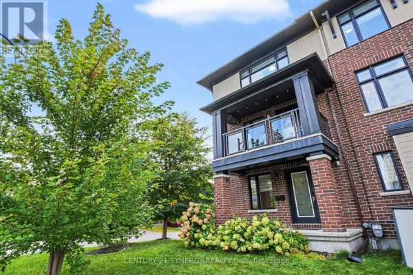Side exterior view of brick townhouse with balcony, glass railing, and front door. - 50 Spicebush Place, Ottawa