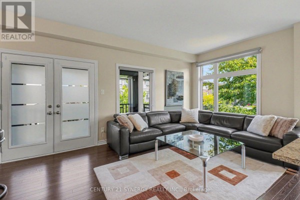 Living room with dark leather sectional, glass coffee table, geometric rug, and double frosted doors. - 50 Spicebush Place, Ottawa