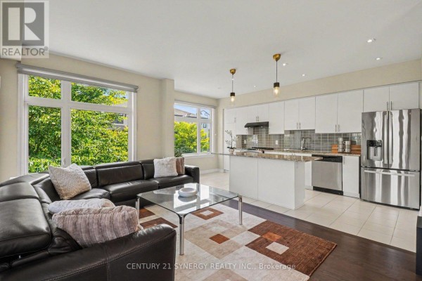 Open concept living room and kitchen with large sectional, island, white cabinets, and stainless steel appliances. - 50 Spicebush Place, Ottawa