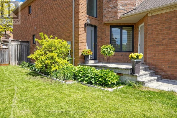 The entrance area of a brick house with stone steps, potted plants, and surrounding green foliage. - 50 Springer Drive, Richmond Hill