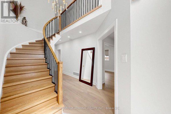 Interior foyer with a curved wooden staircase, black metal railings, hardwood floors, and a full-length mirror. - 50 Springer Drive, Richmond Hill