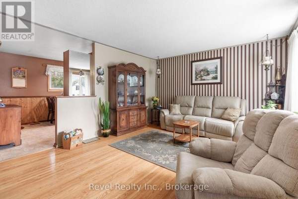 Living room with beige sectional sofa, recliner, wooden hutch, and striped wallpaper. - 50 St David Street, Kawartha Lakes