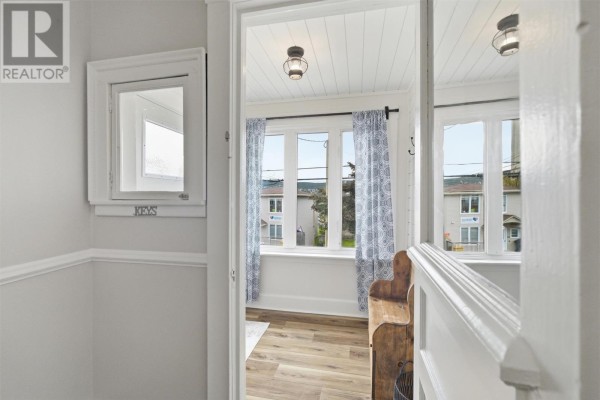 View through an open doorway into a sunroom with patterned curtains and wooden bench. - 50 St. Clare Avenue, St  John S