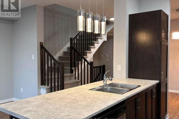 Kitchen island with a double sink and faucet, overlooking a carpeted staircase with dark wood railings. - 50 Stokes Drive, Carleton Place