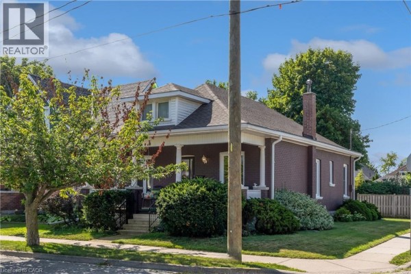 Front porch of a brick house with a mature tree in the foreground and cars parked on the street. - 50 Strathcona Avenue, Brantford