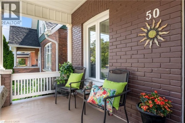 Side view of a red brick house with a porch, white columns, and lush green shrubs. - 50 Strathcona Avenue, Brantford