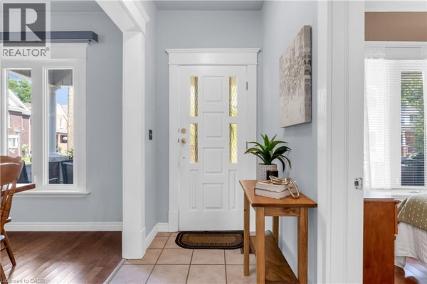 Interior hallway with light blue walls, hardwood floors, doorways to rooms, and a decorative plant on a table. - 50 Strathcona Avenue, Brantford