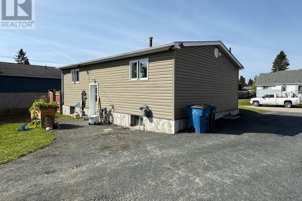 Rear exterior of the house showing a back door, concrete foundation, and gravel area. - 50 Victoria Avenue, Cochrane
