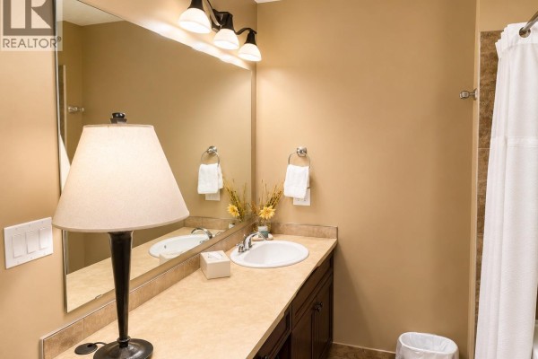 Bathroom vanity with a sink, large mirror, lamp, towels, and a doorway to a bathtub area. - 500 Bighorn Boulevard Unit# 521, Radium Hot Springs