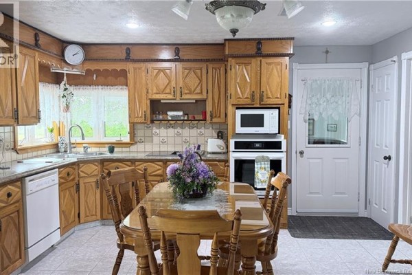 Kitchen with light wood cabinets, tiled backsplash, white appliances, and a wooden dining table with chairs. - 500 Montagne A Comeau, Saint Andre