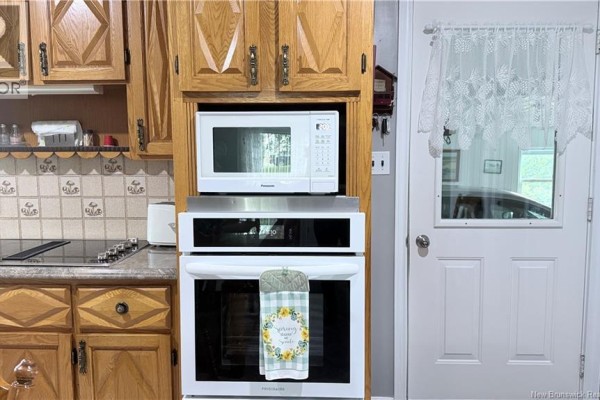 Kitchen area showing a white oven and microwave set into light wood cabinets, with a door to the right. - 500 Montagne A Comeau, Saint Andre