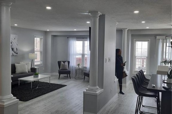 Living room with grey sofa, coffee table, armchair, and windows, connected to a dining area with bar stools. - 500 Snowdrop Court Unit# Upper, Kitchener