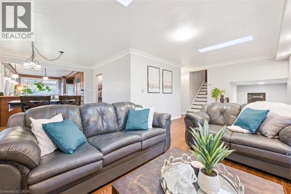 Spacious living room with dark leather sofas, coffee table, and view of stairs. - 500 Watson Parkway S, Guelph