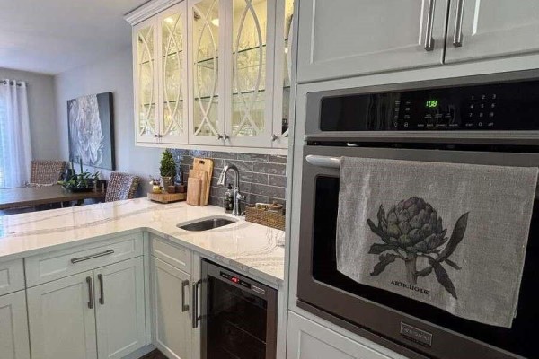 White kitchen with marble countertops, stainless steel oven, and decorative glass-front cabinets. - 5000 Childs Rd, Courtenay