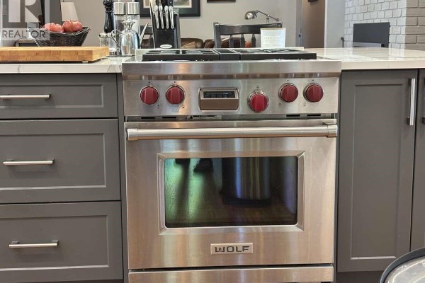Stainless steel Wolf gas range with red knobs and grey cabinetry in a kitchen setting. - 5000 Childs Rd, Courtenay