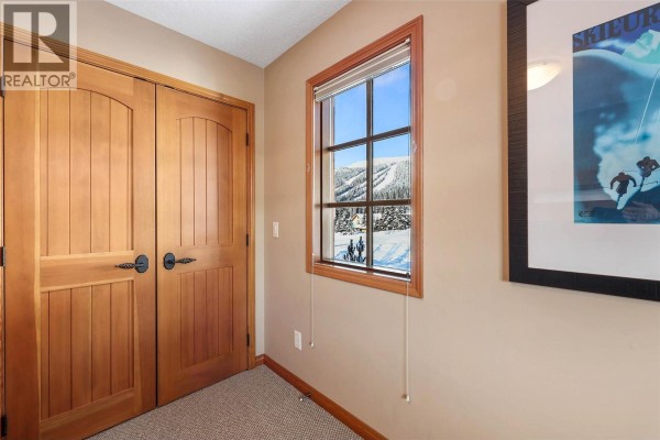 Interior hallway with wooden double doors and a window showing a snowy ski slope view. - 5000 Sun Peaks Road Unit# 1, Sun Peaks