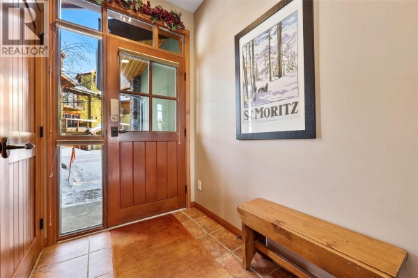Entranceway of a duplex with a wood door, glass panels, tiled floor, and a wooden bench. - 5000 Sun Peaks Road Unit# 1, Sun Peaks