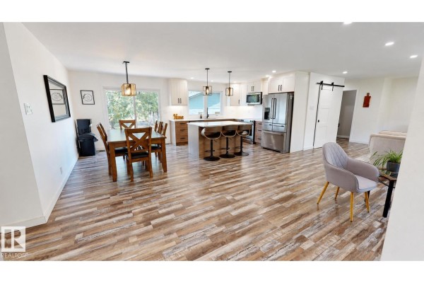 Open concept dining and kitchen area with white cabinets, island, stainless steel appliances, and wood-look flooring. - 50034 Rge Rd 225, Rural Leduc County