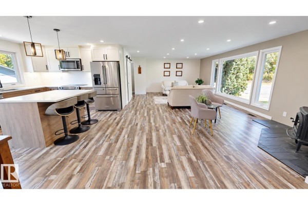 Spacious living room connected to kitchen, featuring large windows, a fireplace, and neutral-toned furniture. - 50034 Rge Rd 225, Rural Leduc County
