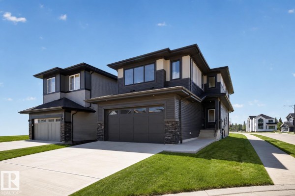 Side exterior view of a dark grey modern two-storey house showing stone accents and windows. - 5004 Cawsey Li Sw, Edmonton