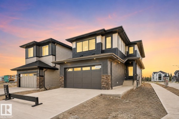 Front view of the house featuring a grey garage door, concrete driveway, and a "For Sale" sign. - 5004 Cawsey Li Sw, Edmonton