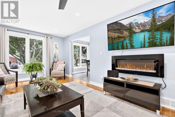 Living room with light grey walls, hardwood floors, a black leather sofa, patterned chairs, and a large rug. - 5004 Pettit Avenue, Niagara Falls