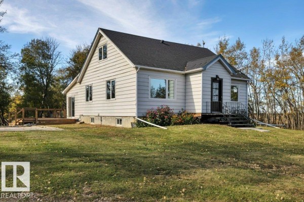View of the side and front of the house, showing the light-colored siding and a wooden deck. - 50040 Rge Rd 230, Rural Leduc County