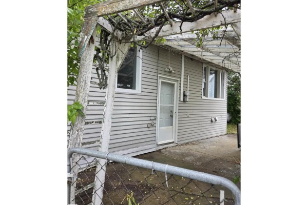 Rear exterior of the house with a white door and a weathered wooden pergola. - 5007 51 Av, Newbrook
