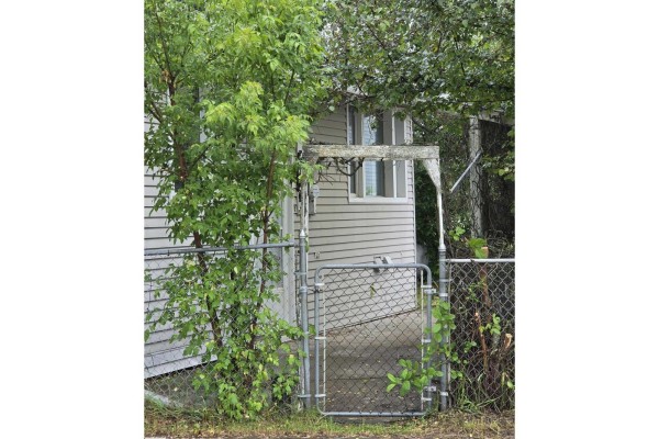 Chain-link gate and fence in front of the house, surrounded by green trees. - 5007 51 Av, Newbrook