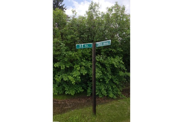 Street signs for 51 Street and 51 Avenue stand at a corner surrounded by trees. - 5007 51 Av, Newbrook