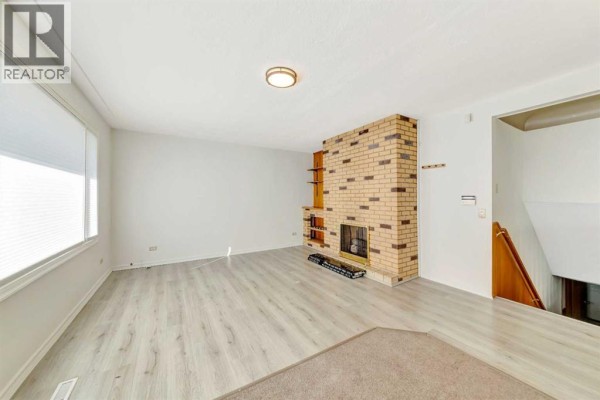 Living area with a brick fireplace, light wood floors, and a view of the staircase. - 5008 47 Street, Lloydminster