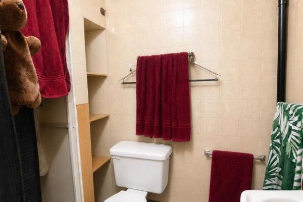 A small bathroom with beige tiled walls, a white toilet, and shelves with burgundy towels. - 5009 52nd Avenue, High Prairie