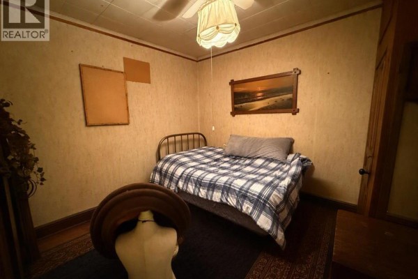 A bedroom with a metal-framed bed, blue and white checkered bedding, and textured wallpaper. - 5009 52nd Avenue, High Prairie