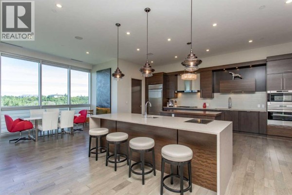 Modern kitchen and dining area with a large island, dark wood cabinets, and red chairs. - 501, 5002 55th Street, Red Deer