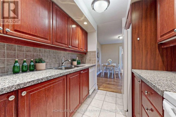 Narrow kitchen with wood cabinets, granite counters, and a view of a dining area. - 501 - 10 Northtown Way, Toronto