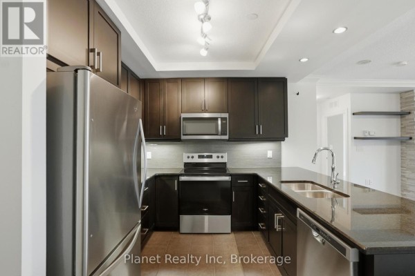 Kitchen with dark cabinets, stainless steel appliances, and granite countertops. - 501 - 150 Wellington Street E, Guelph