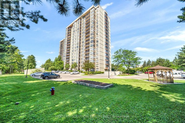 Apartment building with surrounding green space, trees, and a gazebo. - 501 - 20 Cherrytree Drive, Brampton