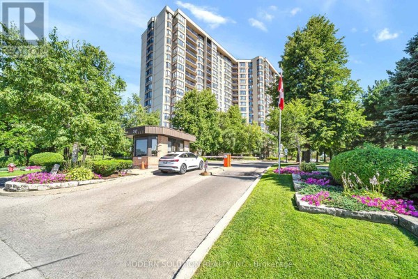 Apartment building entrance with a security booth, gate, and Canadian flag. - 501 - 20 Cherrytree Drive, Brampton