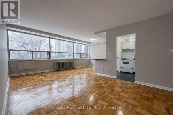 Living area with large window overlooking trees and buildings, parquet floors. - 501 - 42 Thorncliffe Park Drive, Toronto